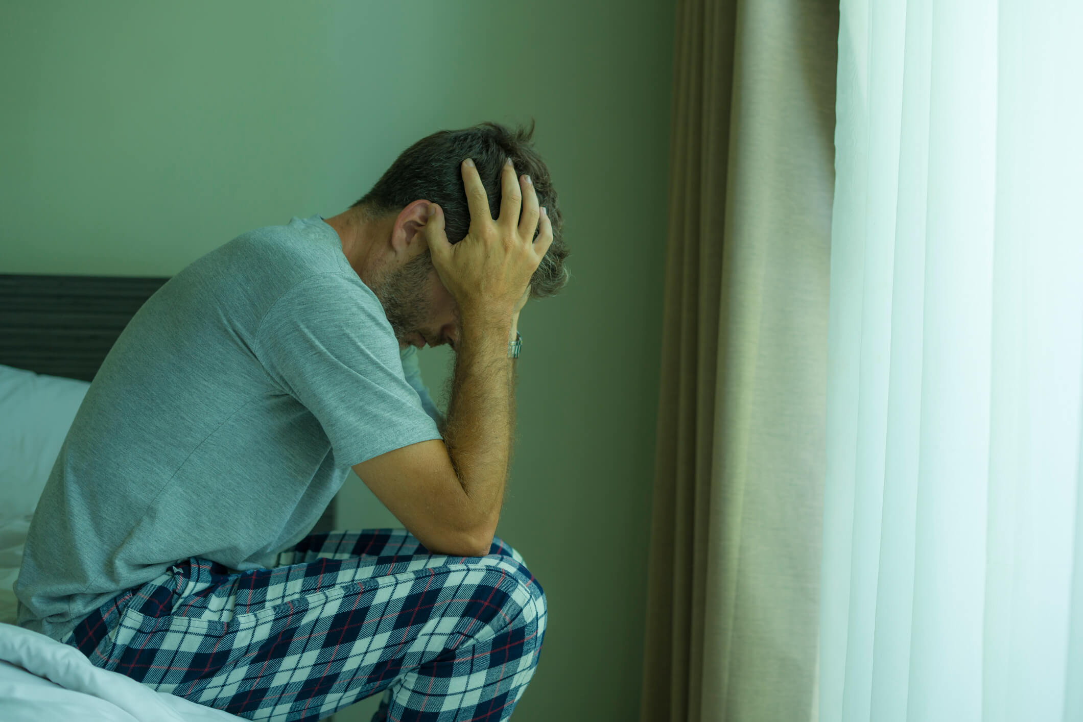 Man sitting on his bed thinking about his alchol abuse