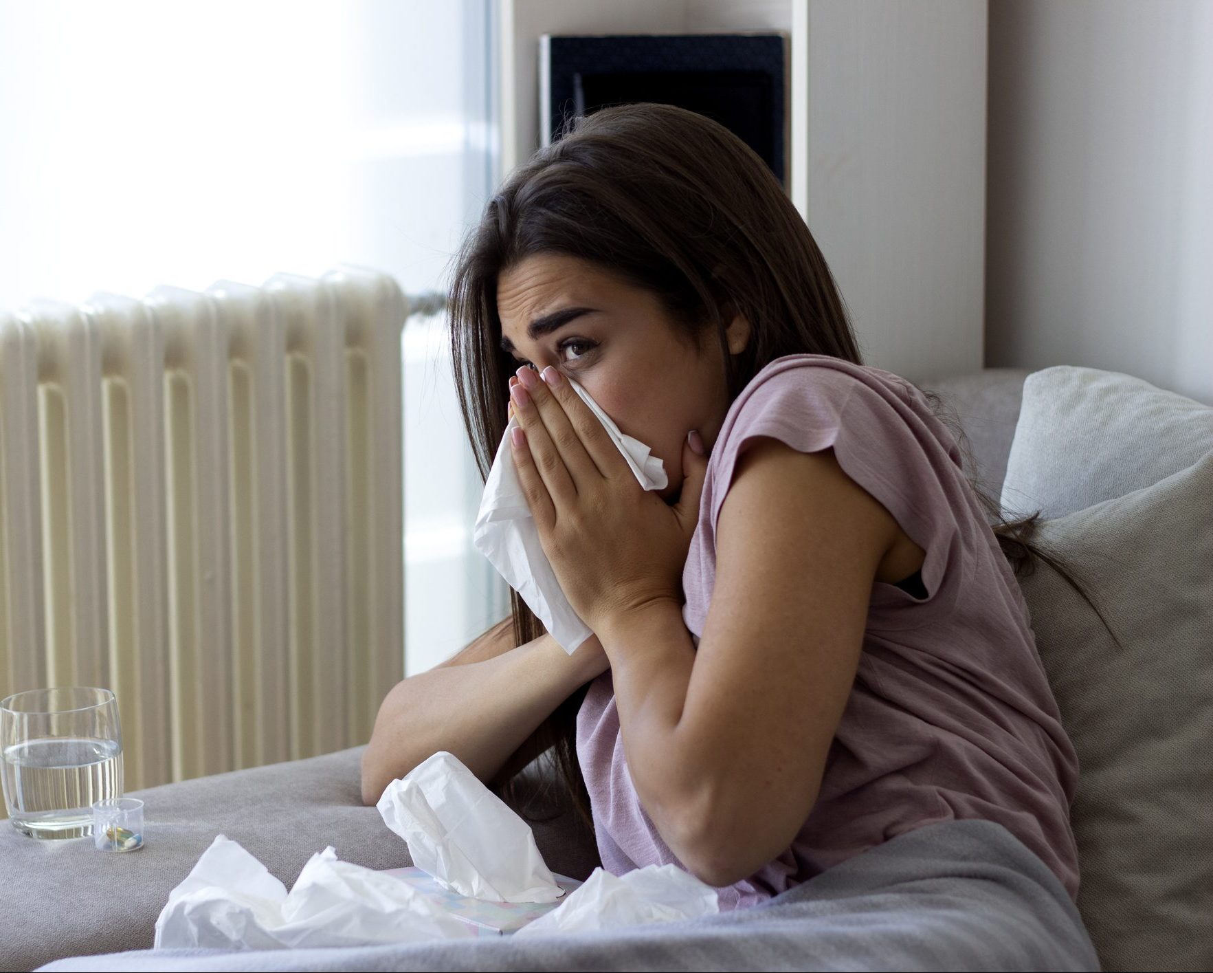 Woman using tissue to sneeze in while being seated at home.