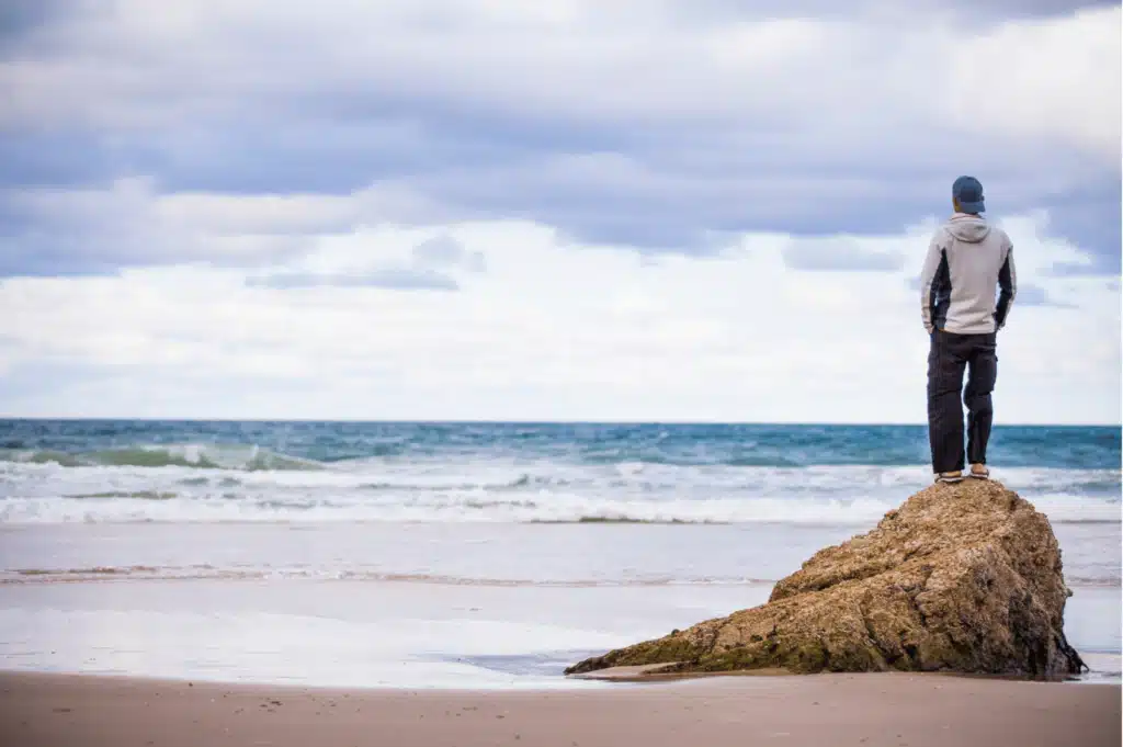 Man standing on rock while looking at ocean