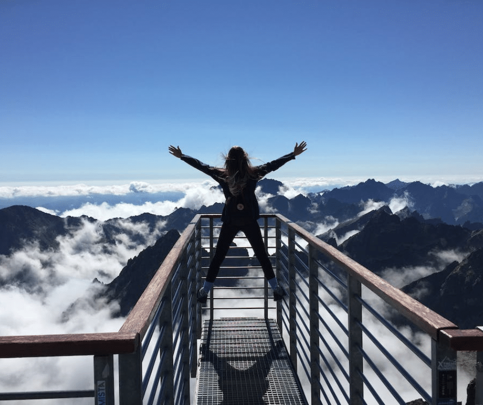 Woman standing triumphantly on a mountain peak with arms extended, symbolizing the achievements of Recovery Month.