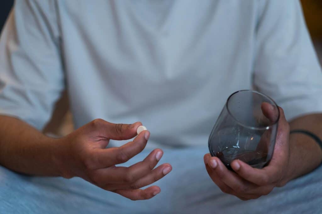 A person holding a glass and a suboxone pill in his hands