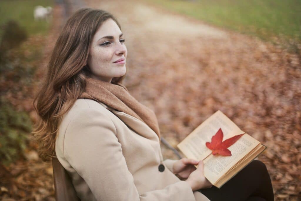 Woman sitting thoughtfully on a park bench, holding a book with a contented smile, symbolizing peace and satisfaction in a moment of solitude.