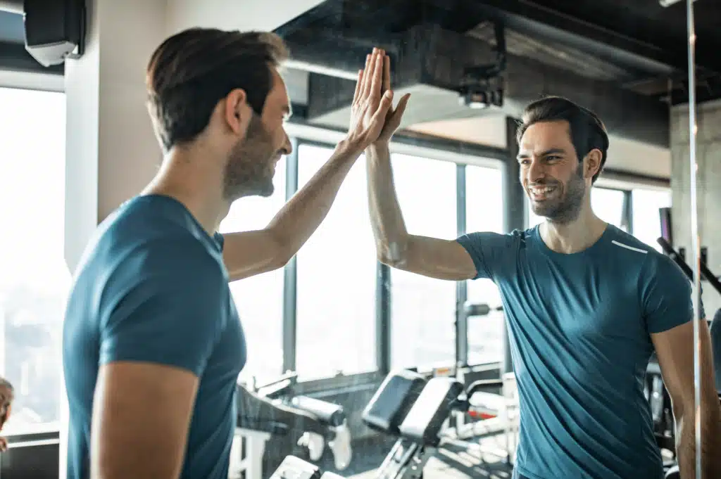 A man high-fives his reflection in a mirror, symbolizing self-efficacy and the importance of believing in yourself to achieve personal goals and maintain a positive mindset.
