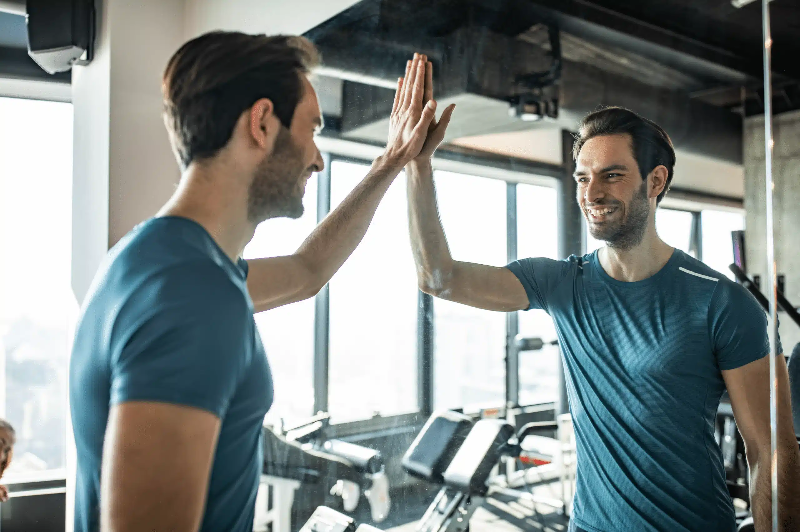 A man high-fives his reflection in a mirror, symbolizing self-efficacy and the importance of believing in yourself to achieve personal goals and maintain a positive mindset.