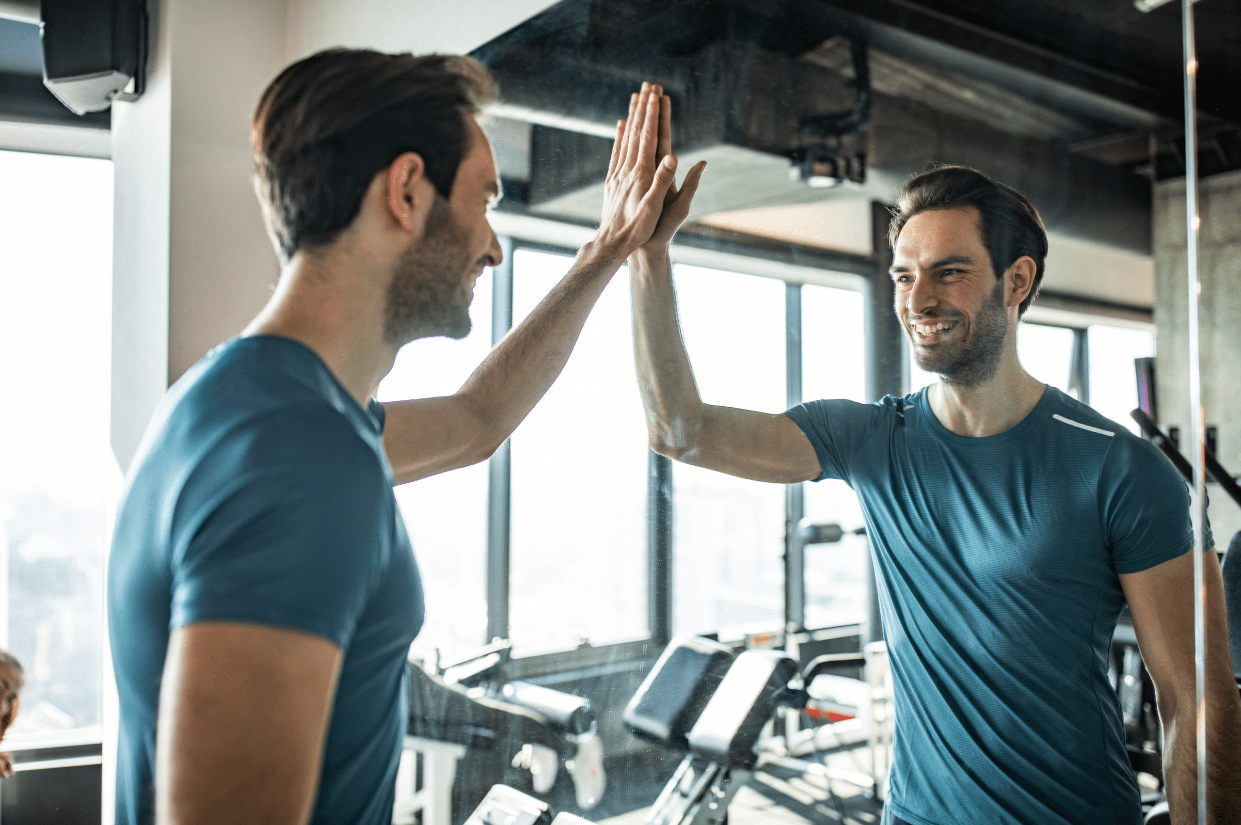 A man high-fives his reflection in a mirror, symbolizing self-efficacy and the importance of believing in yourself to achieve personal goals and maintain a positive mindset.