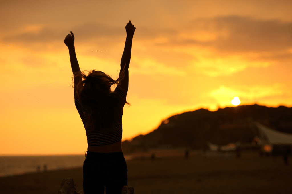 Woman standing triumphantly on a beach with arms extended, symbolizing the achievements of National Recovery Month.